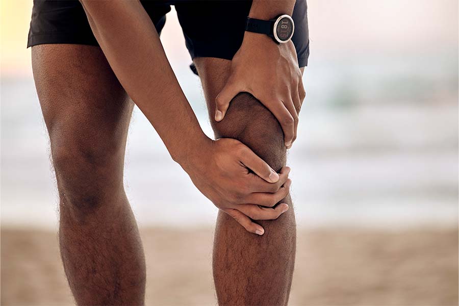 Close de joelho de homem negro com as mão segurando a região. Representação de lesão do ligamento cruzado anterior.