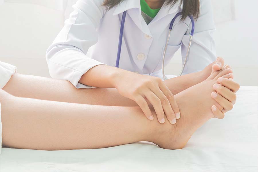Close de uma fisioterapeuta apalpando as pernas de um paciente que está com inchaço decorrente de linfedema.