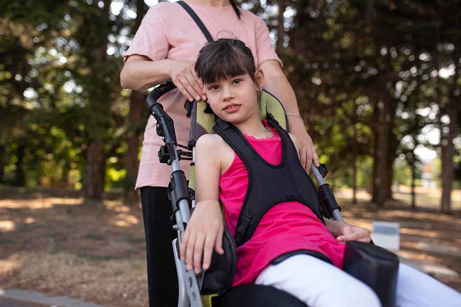 Ao ar livre, menina com paralisia cerebral é empurrada na cadeira de rodas.
