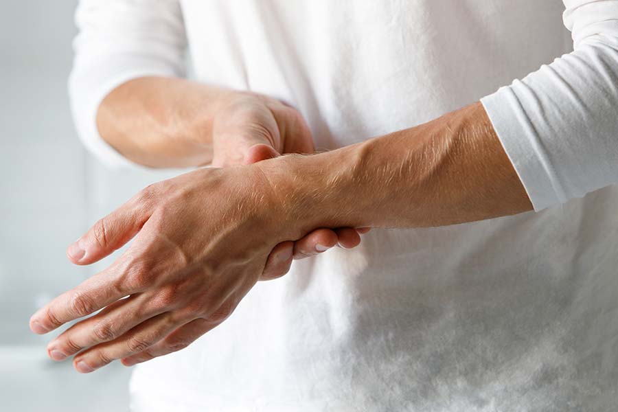 Mulher de branco segurando o punho com uma das mãos por conta de uma artrite reumatoide.