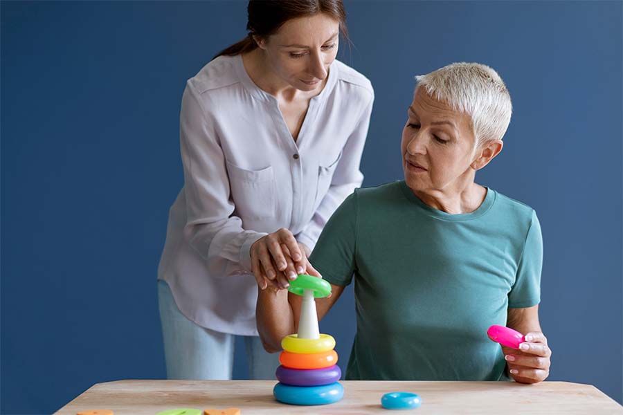 Mulher idosa fazendo exercício de terapia ocupacional com o auxílio de uma terapeuta ocupacional. Representação do papel da terapia ocupacional depois do AVC.