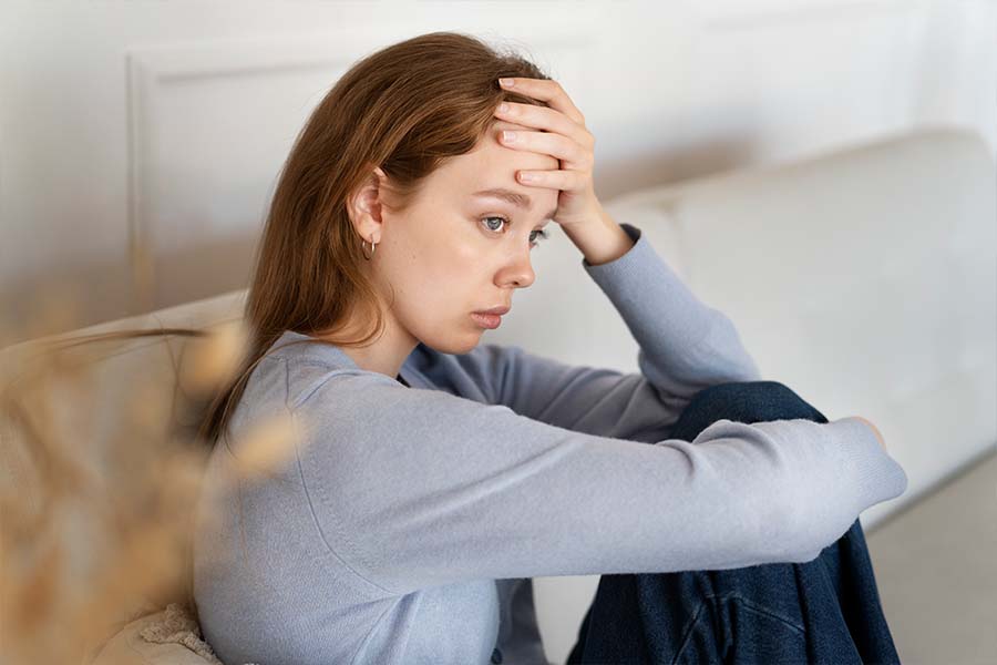 Moça triste sentada no sofá. Ela está com a mão na cabeça indicando ansiedade. Representação dos transtornos de ansiedade.