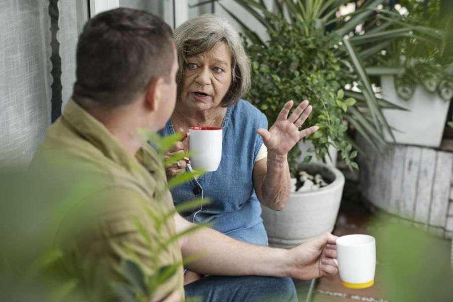 Idoso se comunicando com uma outra pessoa enquanto toma um xícara de chá. Representação de Problemas de comunicação em idosos.