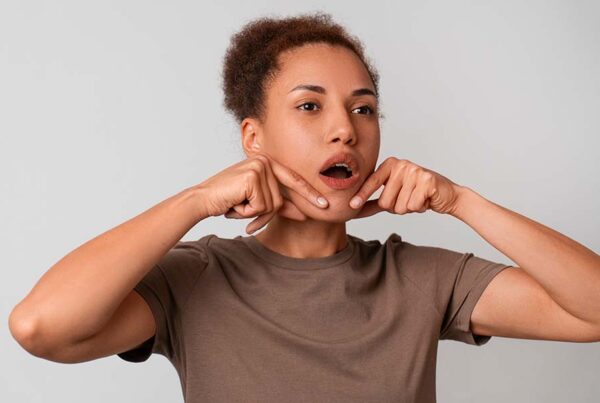 Mulher com as mãos no queixo e a boca aberta em formato de u. Ela está fazendo um fonema, exercício da fonoaudiologia. Representação de tratamentos e ferramentas para distúrbios de linguagem em adultos.